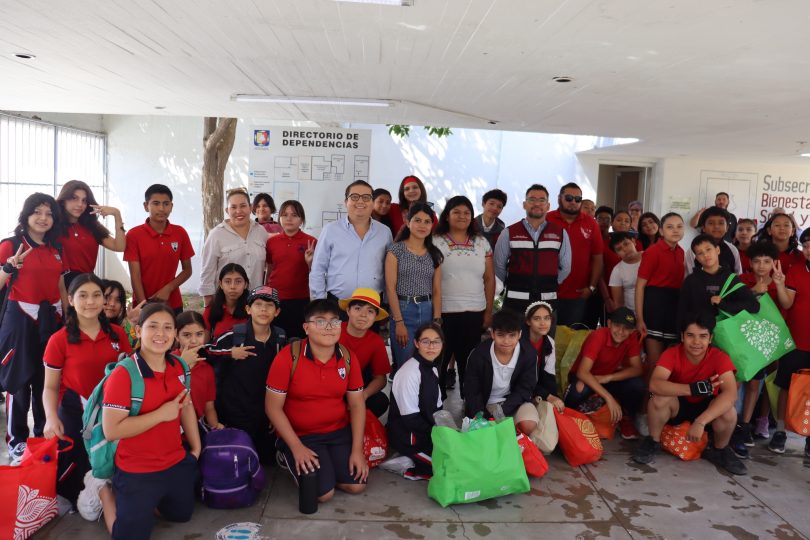 Alumnas y alumnos de la Primaria Benito Juárez posan con sus costales llenos de botellas recicladas junto a personal de la Subsecretaría de Bienestar, momentos antes de depositar el material en el contenedor para botellas PET.